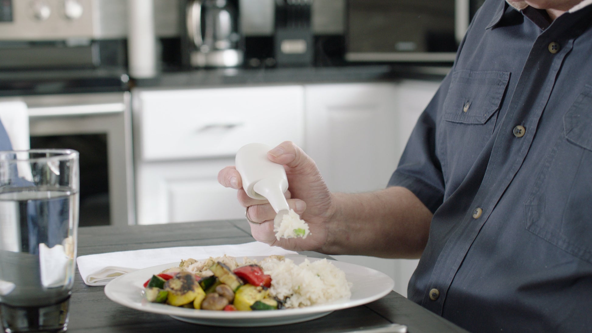 a hand holding Liftware steady with a fork attachmant, eating rice